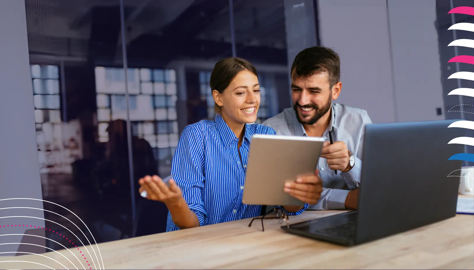 Man and woman sitting down at a table smiling. They are looking at a tablet and a laptop